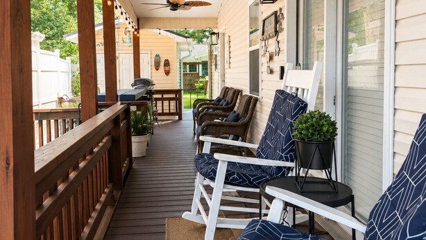 A covered porch with wooden railings, ceiling fans, and outdoor seating with patterned cushions.