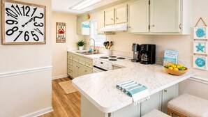 A kitchen with a marble countertop, wooden flooring, and light-colored cabinets.
