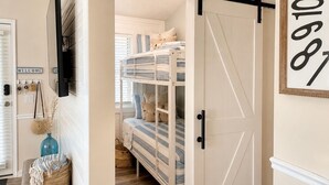 A room with a bunk bed, a sliding barn-style door, a welcome sign, and a blue vase.