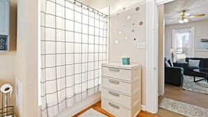 Un baño con cortina de ducha de diseño de cuadrícula, un mueble blanco con cajones y un inodoro a la vista.