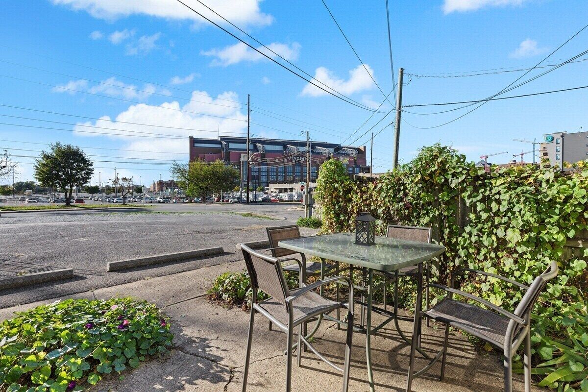 An outdoor seating area with a table and chairs, a hedge, and a building in the background.