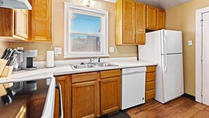Una cocina compacta con armarios de madera, un refrigerador blanco, un lavavajillas y una ventana con persianas.
