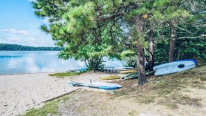 Una playa con kayaks y una canoa cerca de un árbol, un cartel que indica prohibido pescar y un lago tranquilo al fondo.