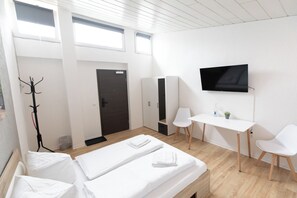 Et hotelværelse med seng, skrivebord, stol, fjernsyn og knagerække.