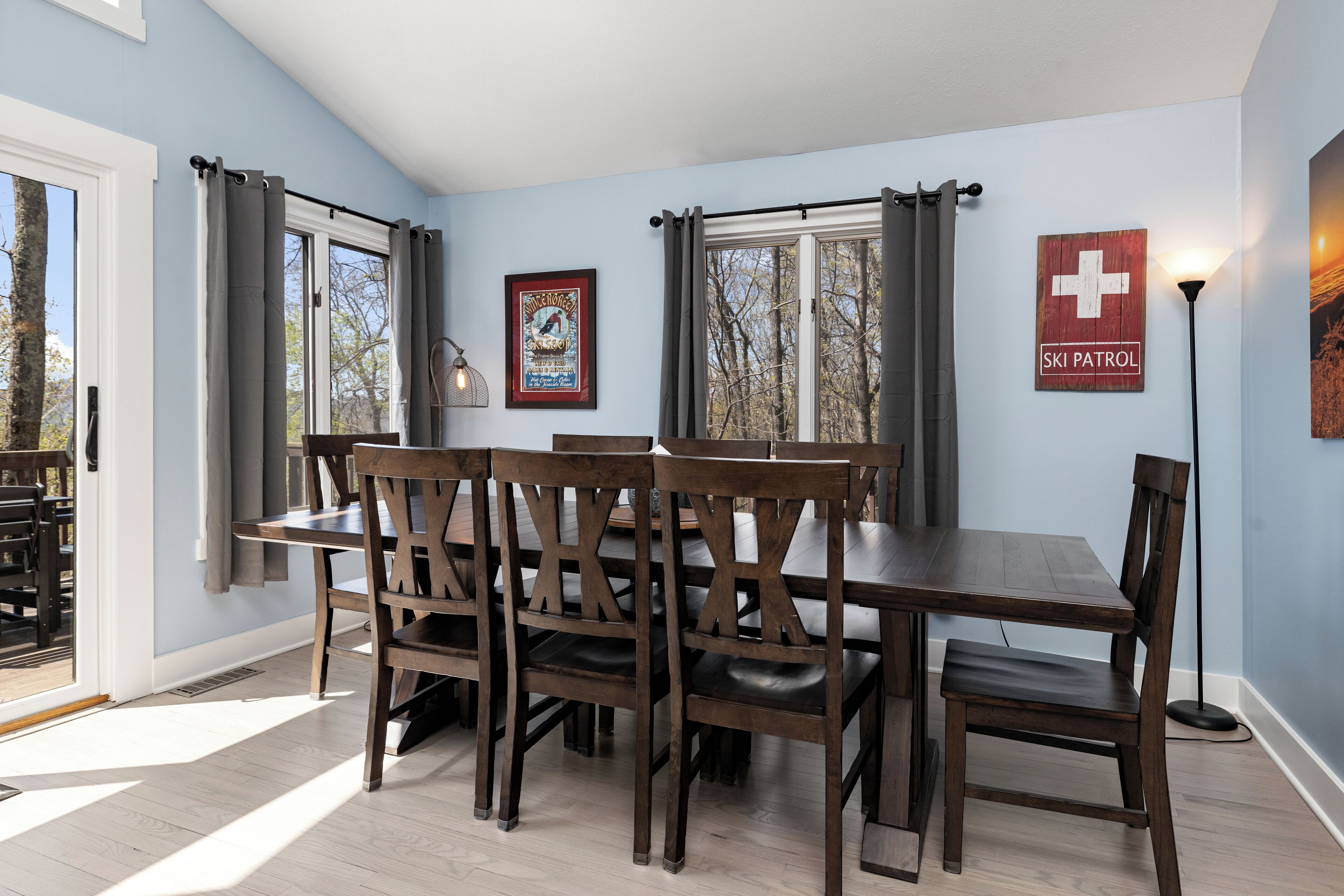 Un comedor con mesa y sillas de madera, obras de arte en las paredes y una ventana con cortinas.