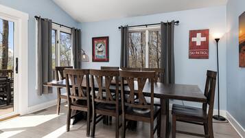 Un comedor con mesa y sillas de madera, obras de arte en las paredes y una ventana con cortinas.