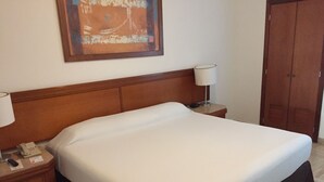A hotel room with a large bed, wooden headboard, bedside tables with lamps, a telephone, and a painting on the wall. - Hotel Sea Garden, Nuevo Vallarta, Mexico. Sleeps 4 adults & 2 children. (Nuevo Vallarta)