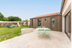 Une terrasse avec une table et des chaises, un jardinier en pierre et un mur en bois avec une fenêtre.