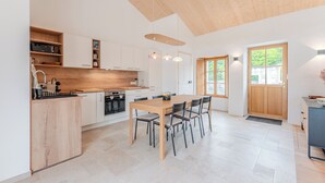 A modern kitchen with a wooden island, white cabinetry, and a dining area with a table and chairs. - Grain d'Or - Proche Noirmoutier - Jardin (Bouin)