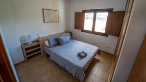 Ein Schlafzimmer mit Bett, Nachttisch, Fenster mit Holzjalousien und Wandbild.
