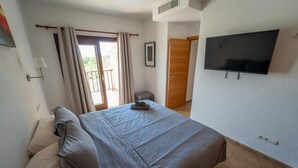 Ein Schlafzimmer mit Bett, Fernseher, Fenster mit Vorhängen und einer Tür.