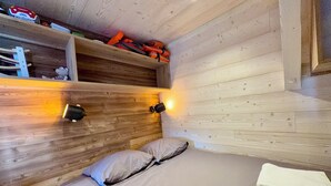 Een kamer met houten lambrisering, een bed, twee wandlampen en een plank met spullen.
