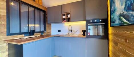 A modern kitchen with a wooden countertop, grey cabinets, a built-in oven, and a painting on the wall.