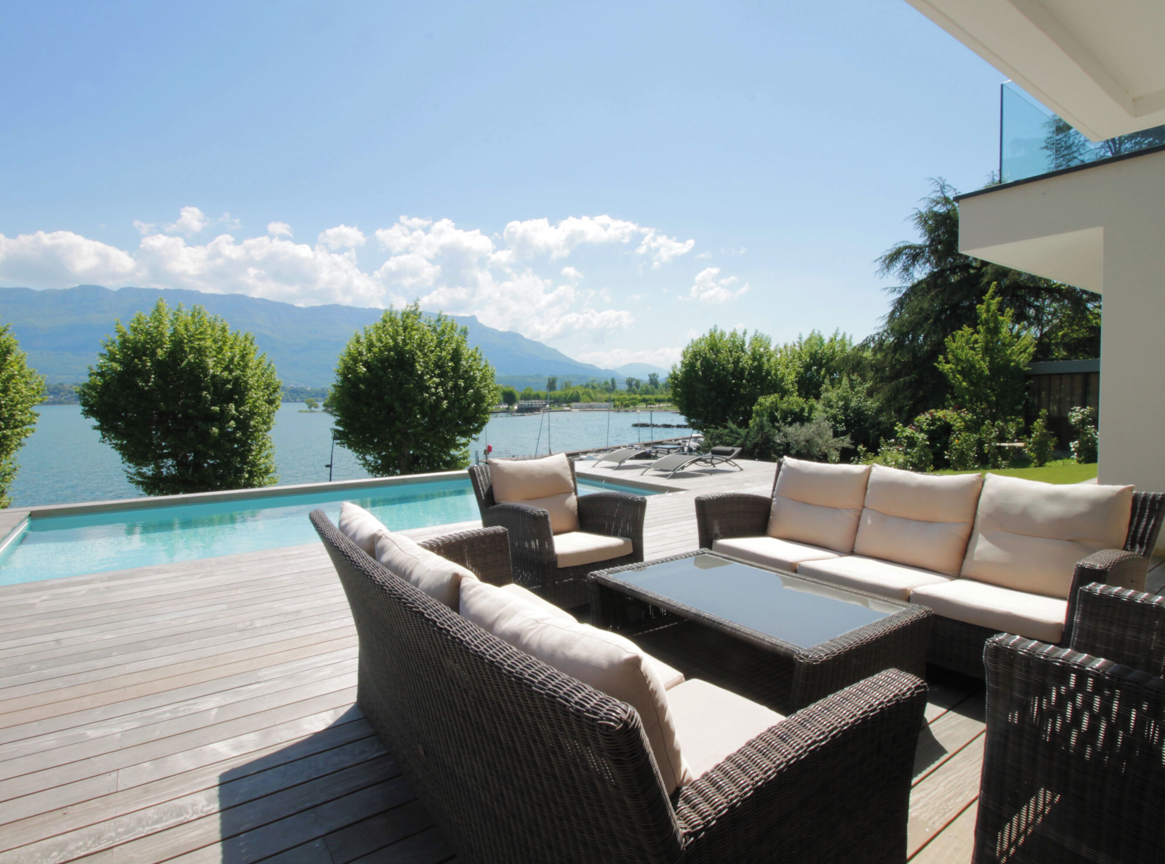 An outdoor deck with a pool, wicker furniture, and a view of a lake and mountains.