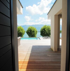An outdoor wooden deck with a pool and lounge chairs, overlooking a lake and mountains. - Villa Piscine chauffée, vue et accès lac, climatisation (Le Bourget-du-Lac)