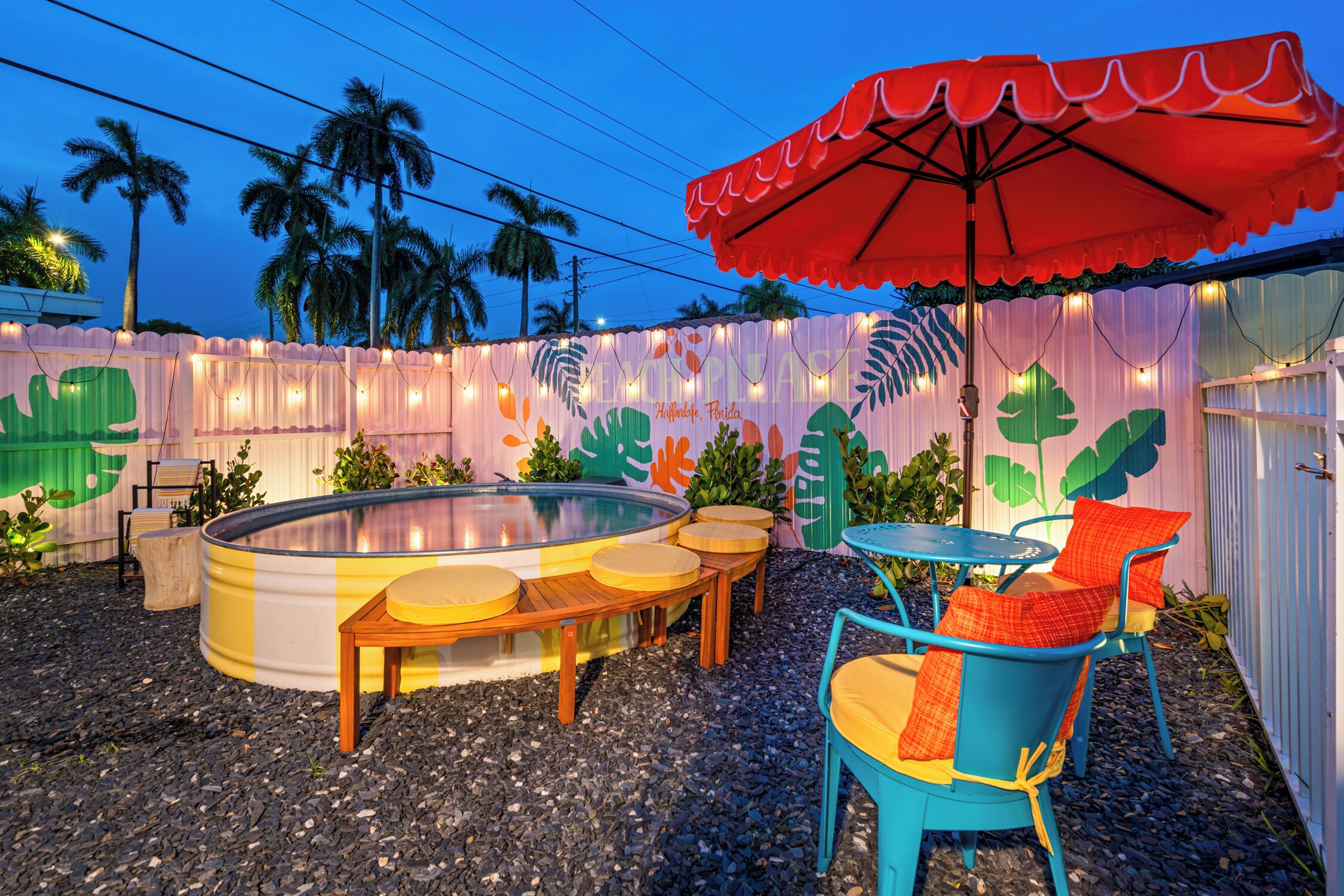An outdoor pool area with a hot tub, wooden deck seating, and a table with chairs.