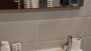 Un baño con lavamanos blanco, artículos de tocador y un espejo.