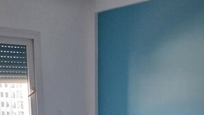 Un dormitorio con una cama, una ventana, pared azul y alfombra estampada.