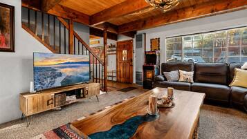 A spacious living room with a wooden coffee table, a large flat-screen TV, a leather sofa, and a staircase with wooden railings.