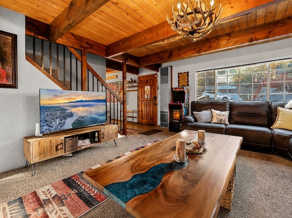 A spacious living room with a wooden coffee table, a large flat-screen TV, a leather sofa, and a staircase with wooden railings.