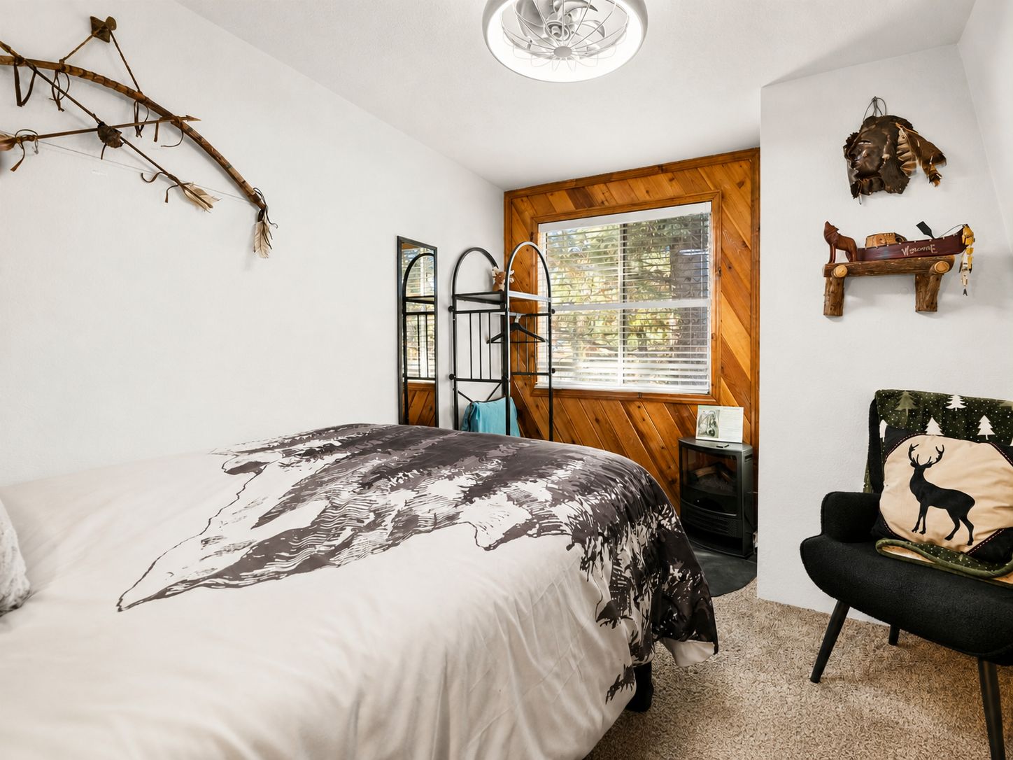 A bedroom with a bed, a chair, a window, and a wall-mounted shelf.