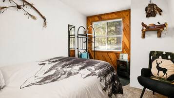 A bedroom with a bed, a chair, a window, and a wall-mounted shelf.