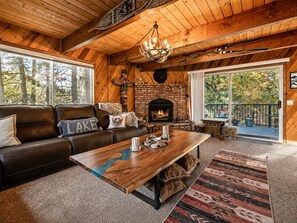A cozy cabin interior with a fireplace, leather sofa, and a dining table. - Birdhouse in Moonridge (Big Bear City)