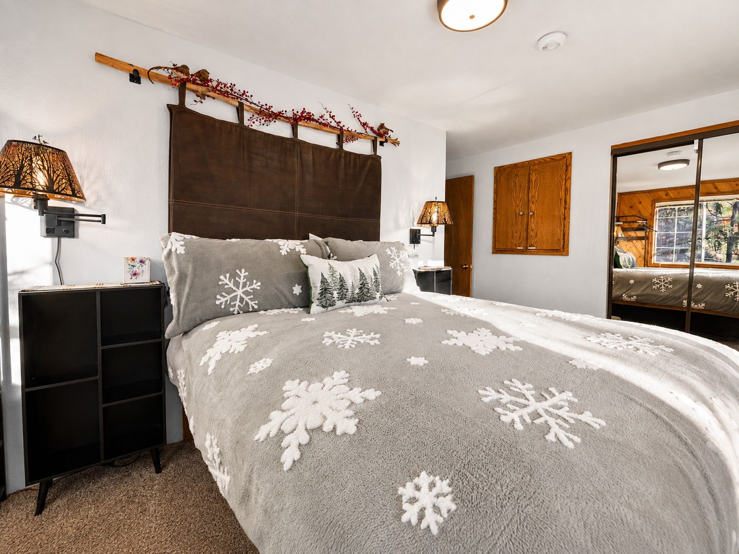 Une chambre à coucher comprenant un lit, une table de chevet, une lampe, un miroir et une fenêtre donnant sur des arbres.