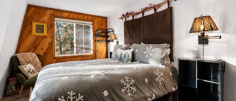 Une chambre avec un grand lit, une tête de lit en bois, une fenêtre donnant sur un beau paysage, une table de chevet avec une lampe et une chaise avec une couverture.