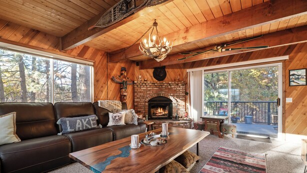 Un interior de cabaña acogedor, con chimenea, sofá de cuero, mesa de centro de madera y ventanas amplias.