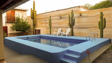 An outdoor swimming pool with a blue border, white chairs, and cacti painted on the wall.