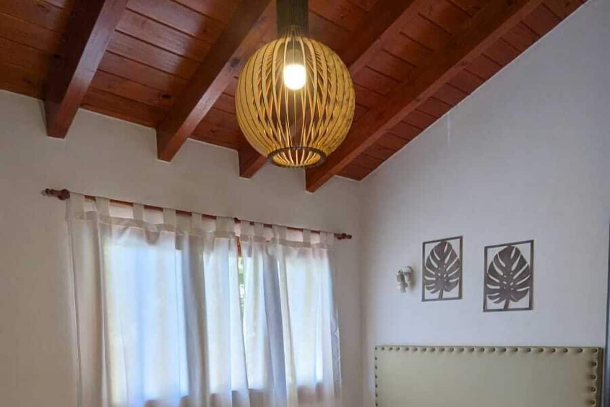 A bedroom with a bed, curtains, a hanging light fixture, and two wall decorations.