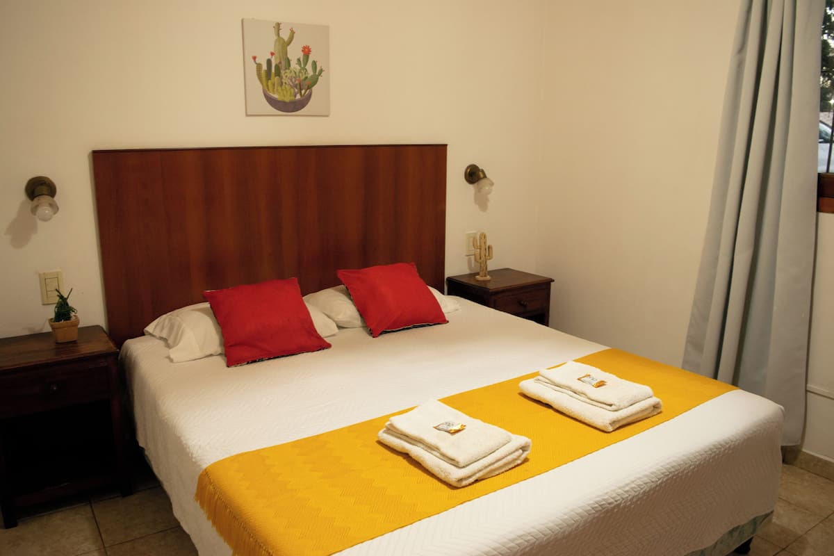 A neatly made bed with a wooden headboard, two red pillows, and a yellow bedspread. There are two white towels folded on the bed.