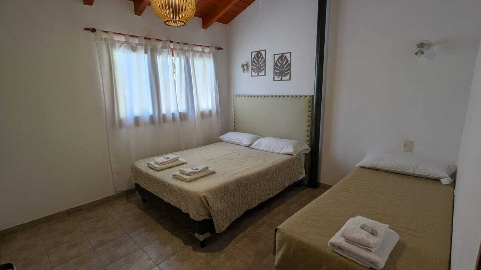 Une chambre avec deux lits, une fenêtre avec des rideaux, un ventilateur de plafond et des œuvres d’art murales.