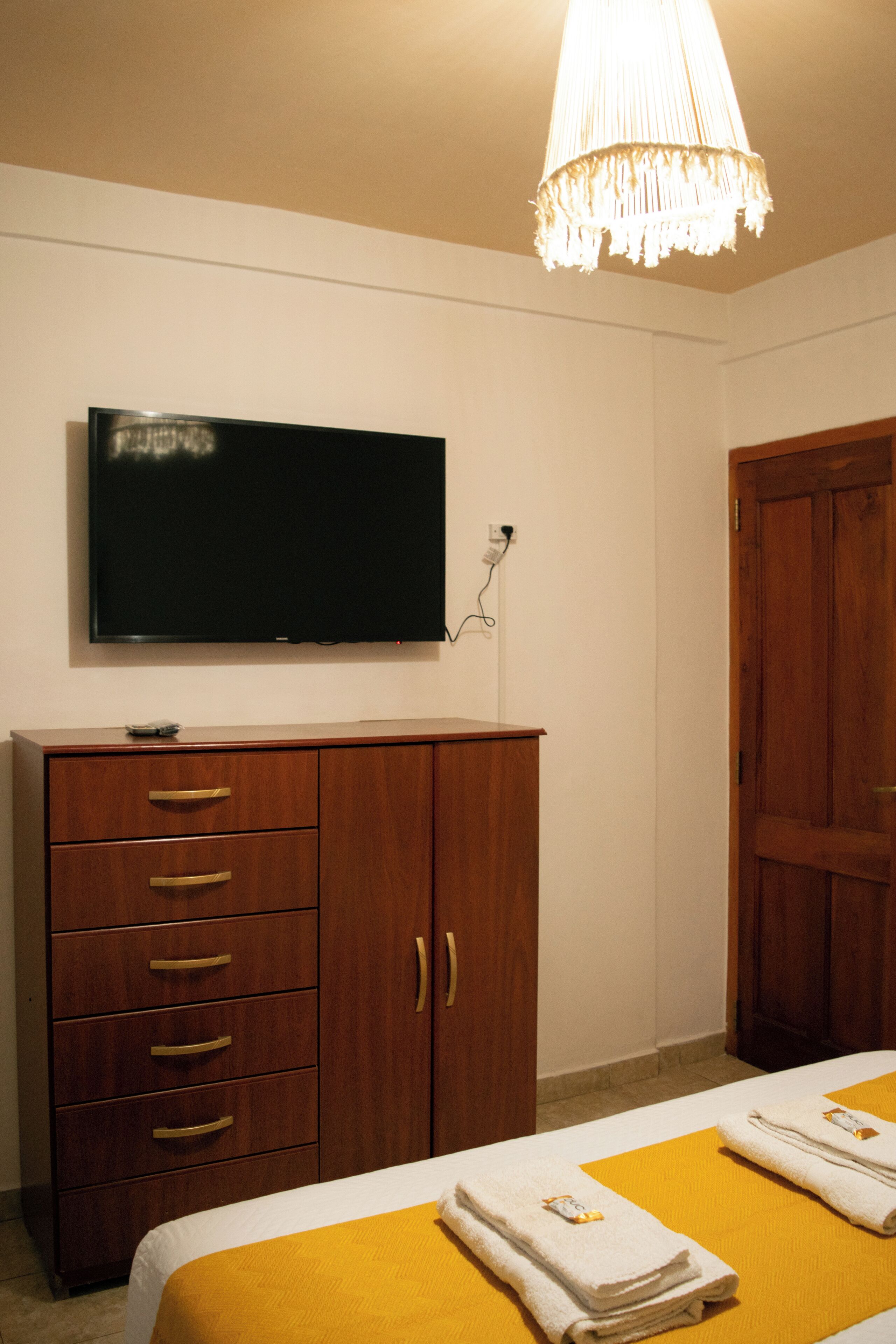 Una habitación de hotel con una cama, un televisor en la pared, un armario de madera y una puerta.