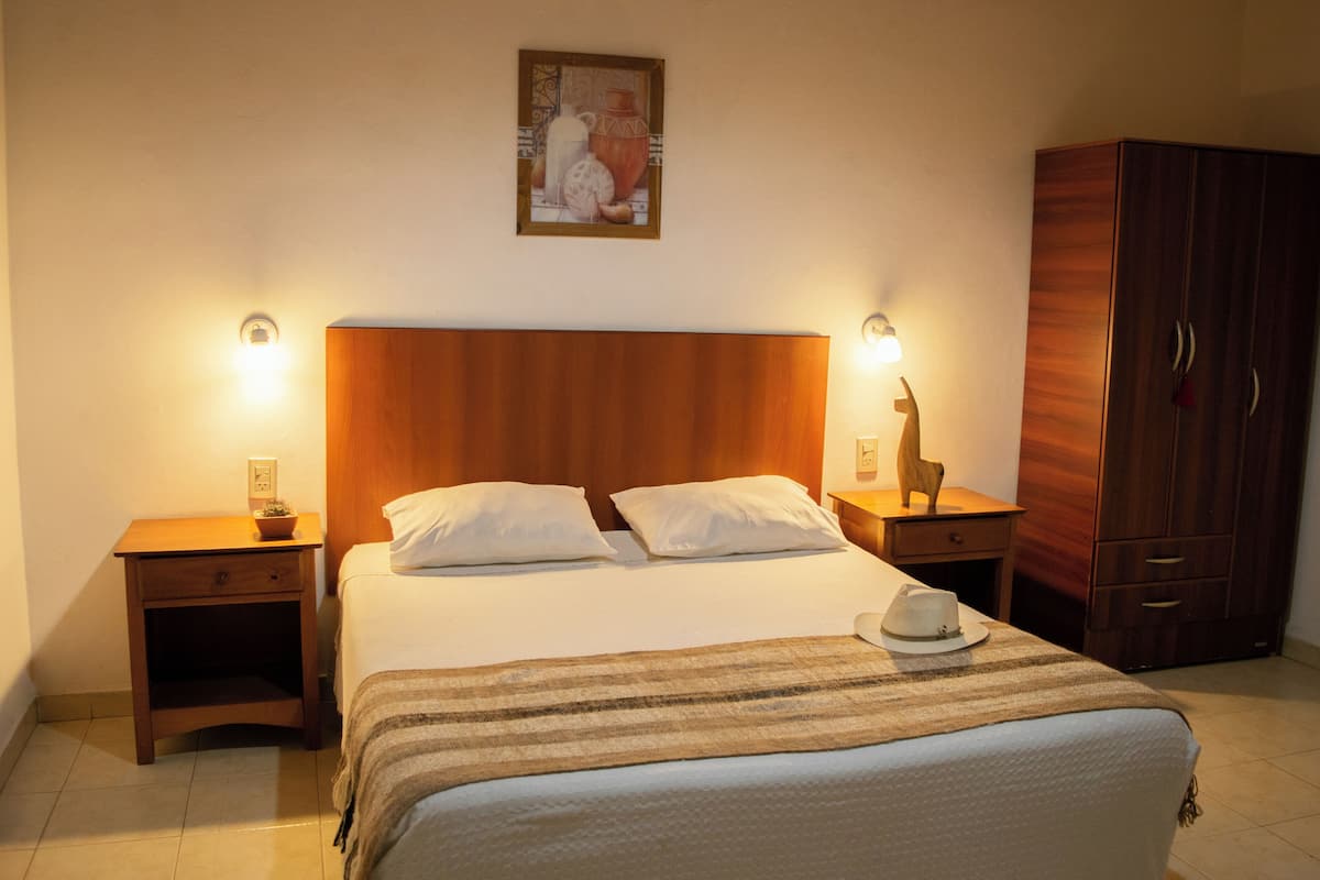 A neatly made bed with two pillows, a wooden headboard, bedside tables with lamps, and a wardrobe.