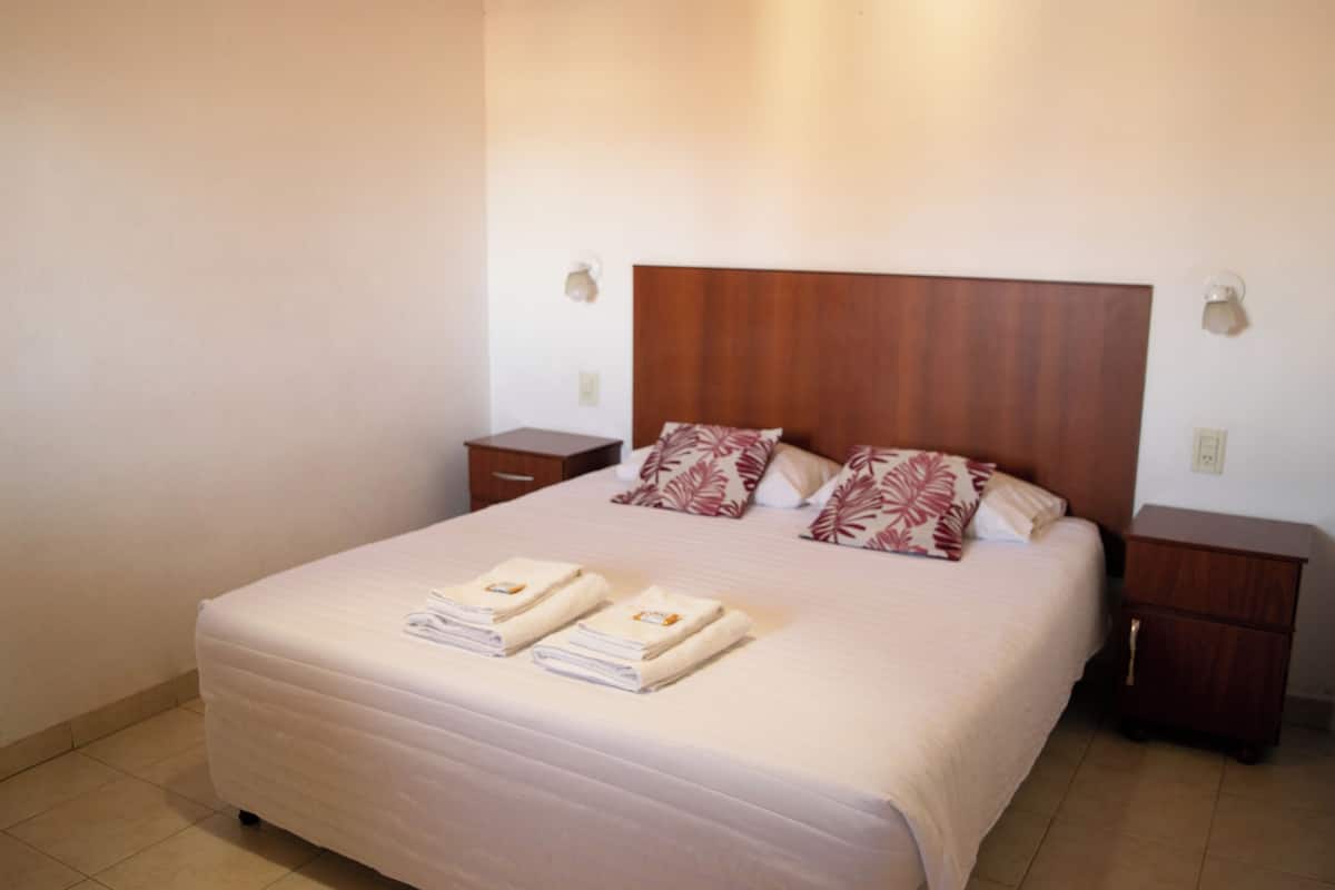 A neatly made bed with pillows, a wooden headboard, and two bedside tables with lamps.