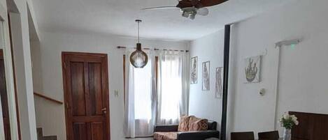A spacious living area with a ceiling fan, a dining table with chairs, a sofa, and a staircase leading to another level.