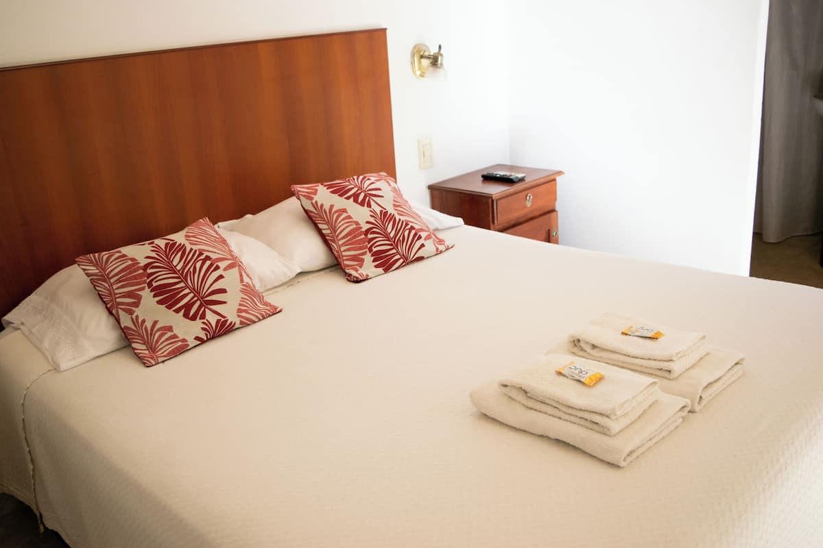 A neatly made bed with a wooden headboard, two pillows with a leaf pattern, and two folded towels with a tag.