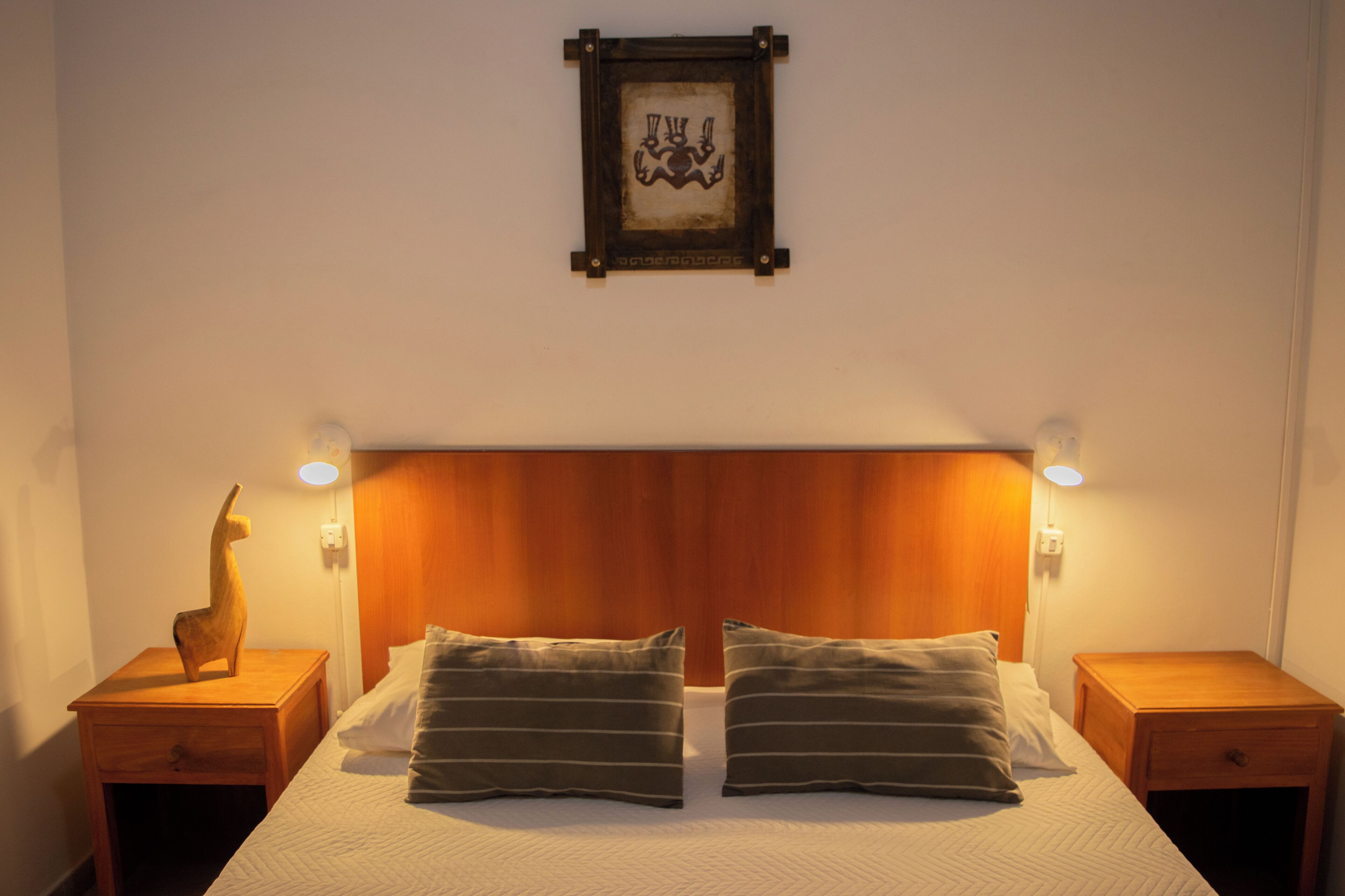A neatly made bed with two pillows, a wooden headboard, and two bedside tables with lamps.