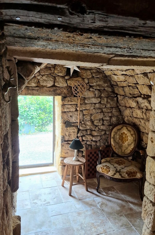 A rustic room with a stone wall, a checkered chair, a lamp, and a patterned table.