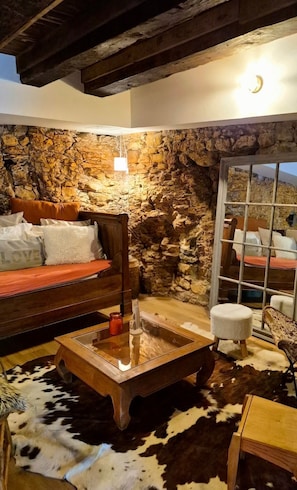 A rustic interior with a stone wall, a wooden bed, a glass coffee table, and a cowhide rug.
