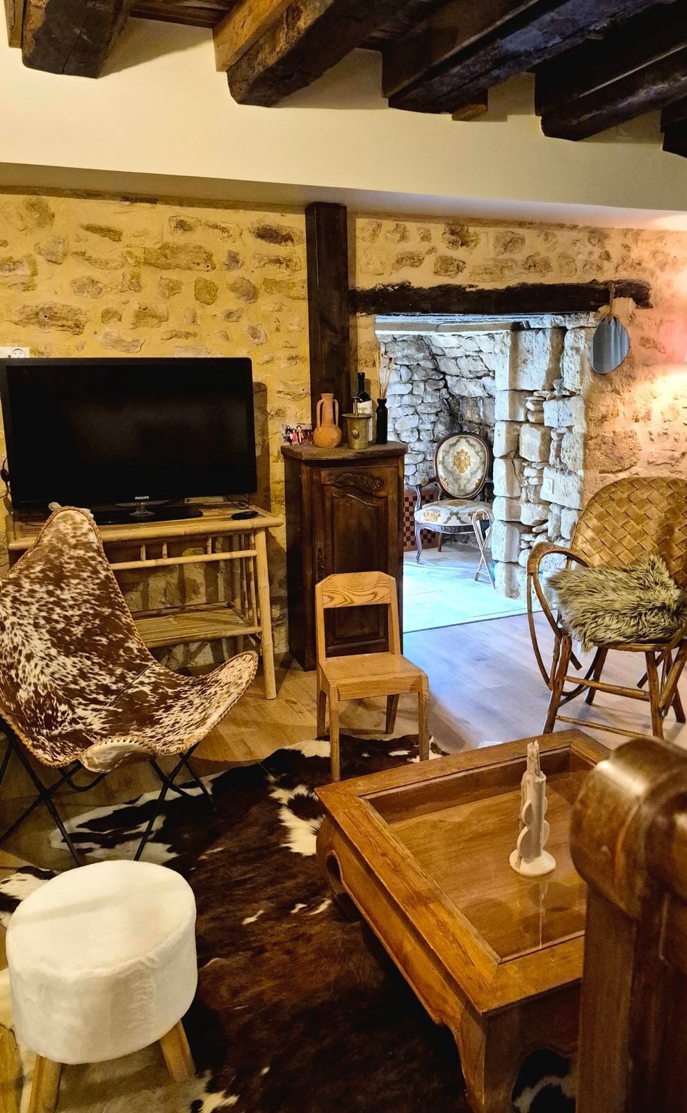 A rustic living room with a television, a patterned chair, a small table, and a stone fireplace.
