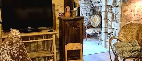 A rustic living room with a television, a patterned chair, a small table, and a stone fireplace.