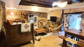 Un intérieur rustique avec des murs en pierre, un canapé en bois, une table à manger et un téléviseur.