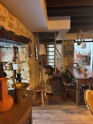 A rustic interior with stone walls, a wooden staircase, and a dining area with a table and chairs.