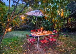 An outdoor dining area with a table and chairs, surrounded by trees and a grassy lawn.