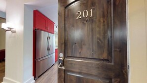 A wooden door with the number 201, a stainless steel refrigerator, and a red cabinet in the background.