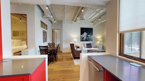 A modern hotel room with a kitchen area, a dining space, and a living area with a large window.