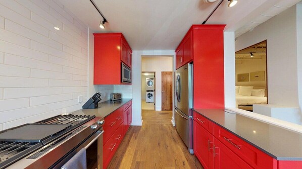A modern kitchen with red cabinetry, a stainless steel refrigerator, and a built-in oven. - The Lincoln 201, 2 Bed / 2, Bath Luxury Loft Style Condo (Santa Fe)